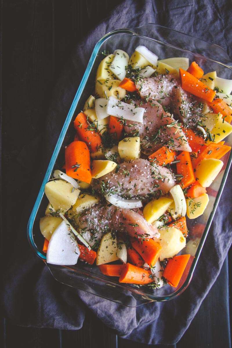Baked chicken, potatoes, carrots and herbs in a glass baking dish