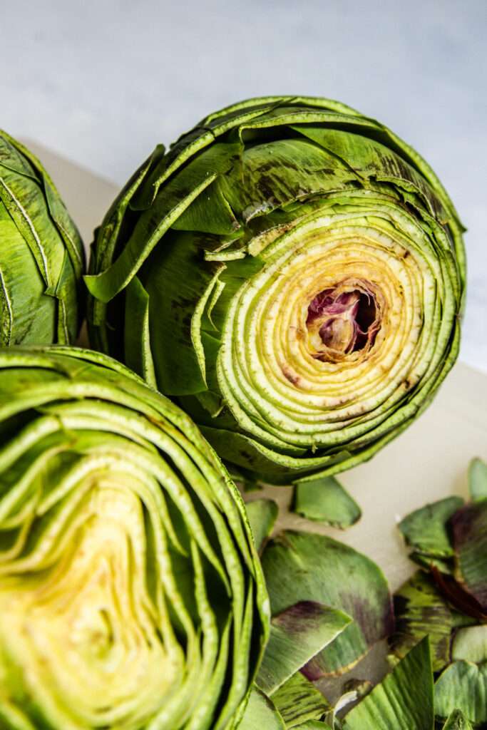 Cleaned artichoke with tip cut off on a white cutting board