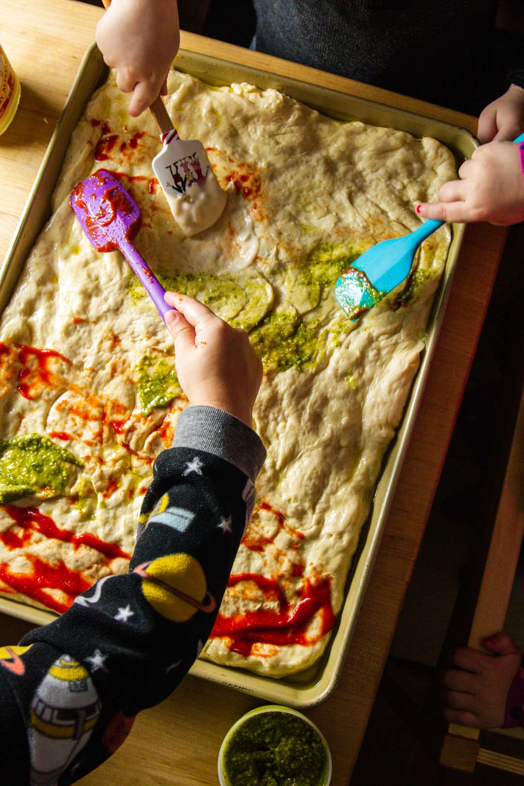 Kids spreading pizza sauce on dough