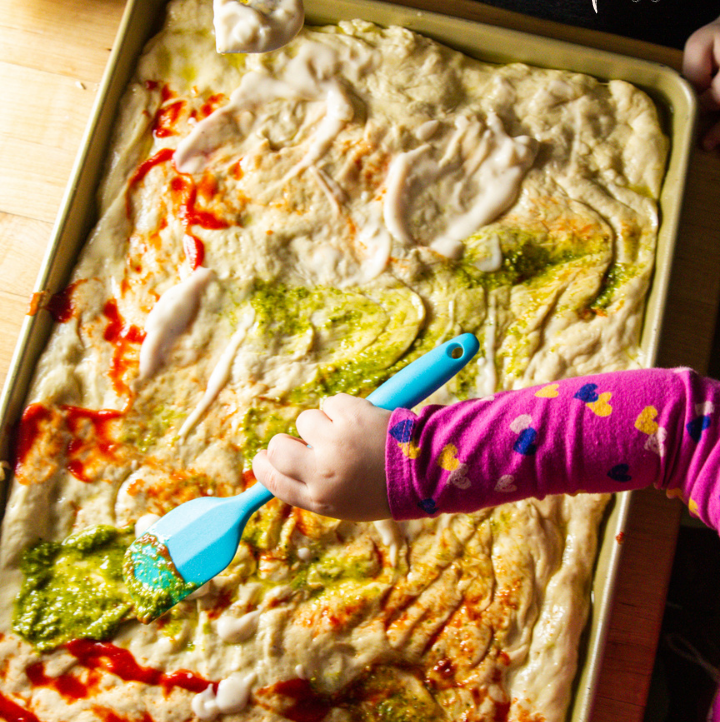 Kids spreading three sauces on pizza dough