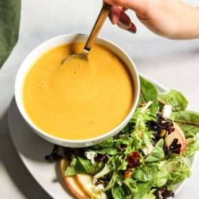 Butternut squash soup in a white bowl with a side of salad